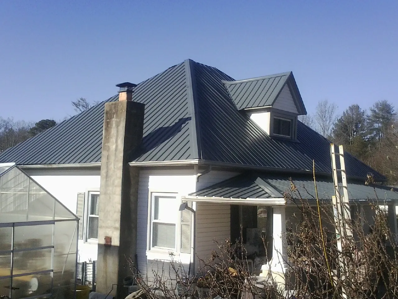 Dark blue standing seam metal roof on a white farmhouse with dormer — Slate & Tile Roof Repair by Roofing Brothers in Medicine Bow