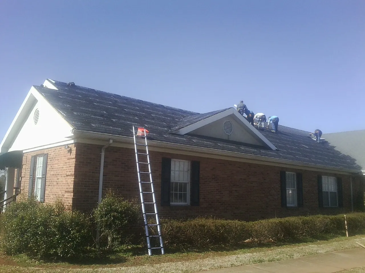 Crew tearing shingles off a brick ranch roof with a ladder set — Emergency Roof Repair work by our crew in Medicine Bow