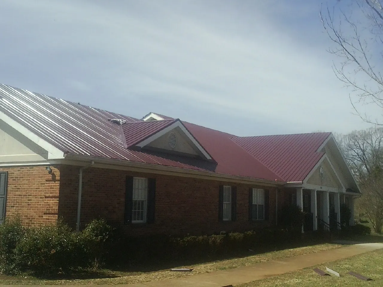 Red metal roof with gabled entries on a long brick building, from a Hail Damage Roof Repair job in Medicine Bow