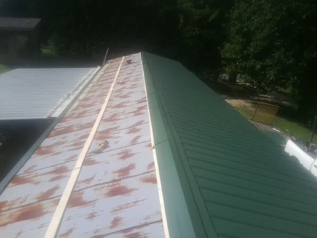 Old rusted panels beside newly installed green metal roofing — Wind Damage Roof Repair by Roofing Brothers in Medicine Bow