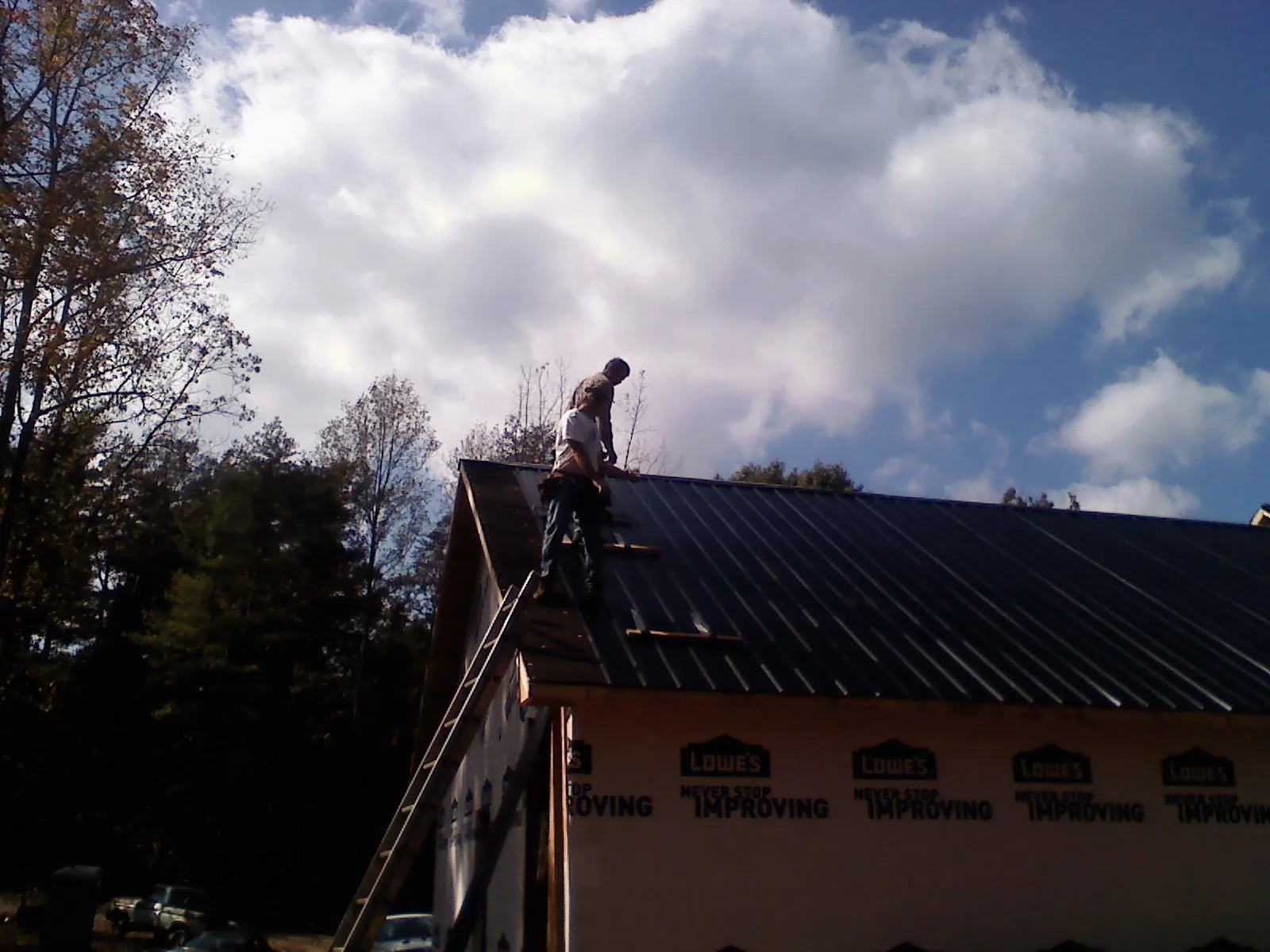 Roofer fastening dark metal panels high against a cloudy sky, from a Roof Inspection job in Medicine Bow