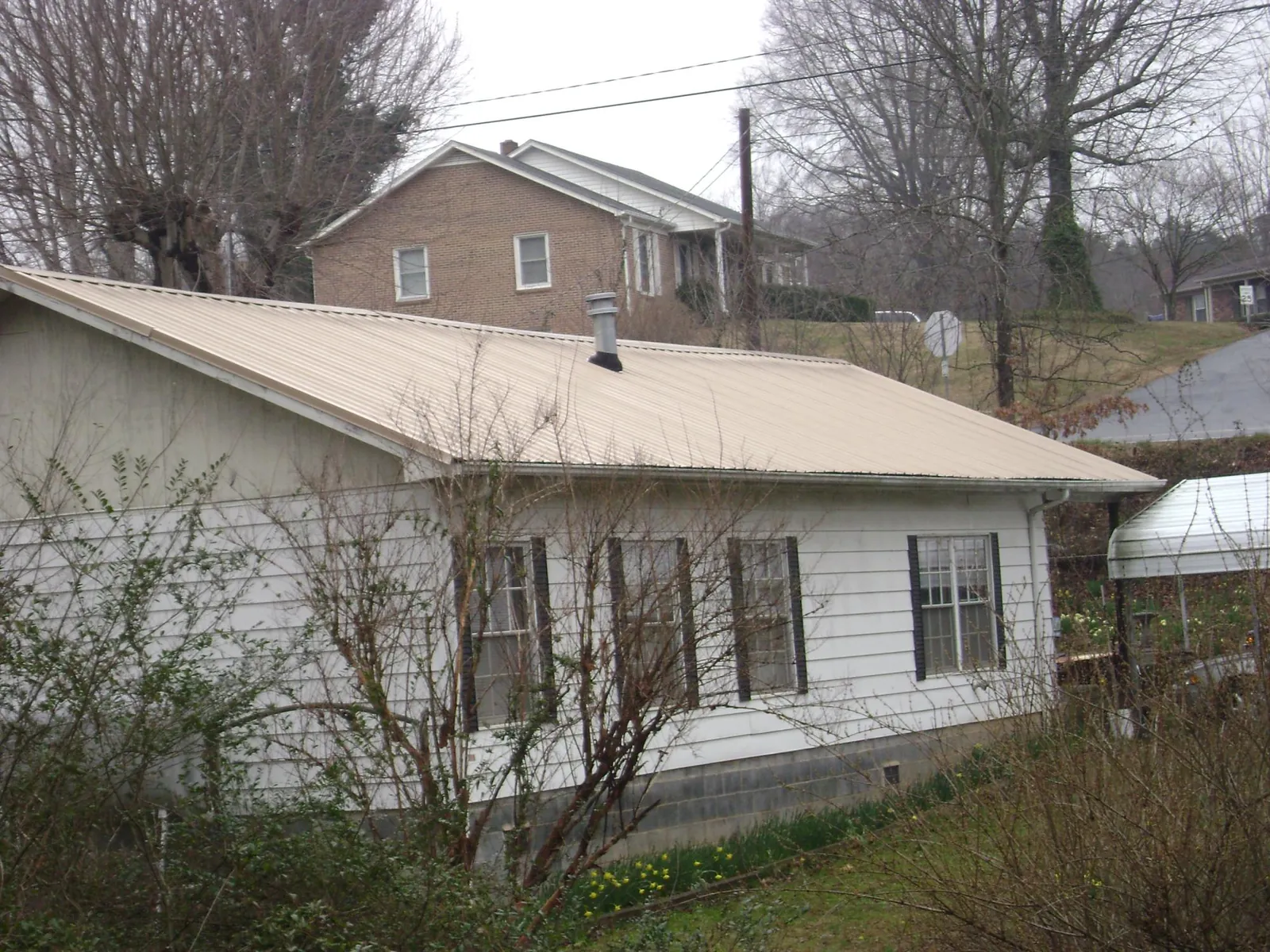 Tan metal roof on a white sided house set into a hillside — Commercial Roofing by Roofing Brothers in Medicine Bow