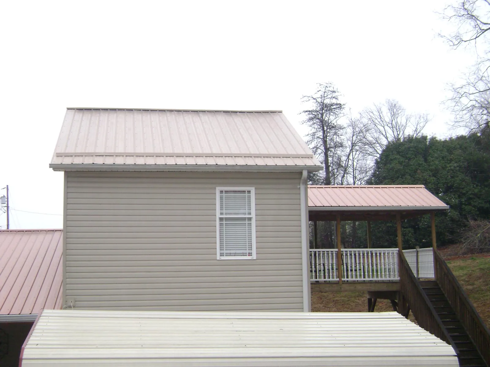 Tan metal roofs on a two story addition and attached porch, from a Roof Replacement job in Medicine Bow